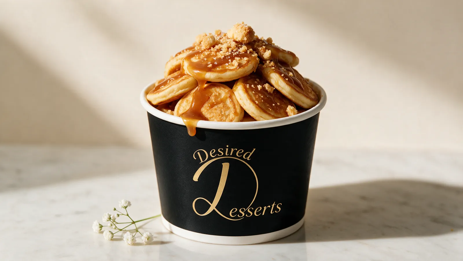 Desired Desserts mini pancakes with shortcake crumble and salted caramel drizzle in a black branded tub.